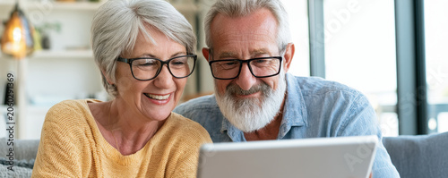 Senior couple happy senior retired people digital tablet home living room modern glasses grey hair casual sweater smiling face soft daylight senior man senior woman elderly couple mature adult