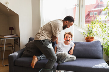 Playful father tickling laughing son on sofa