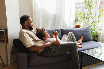 Relaxed father and son resting on sofa with phone