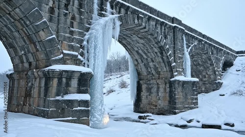 Dramatic Icicles Hang from Historic Stone Arch Bridge in Winter Snowfall