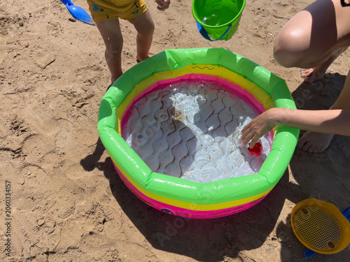 Children and adult playing by inflatable pool on sand