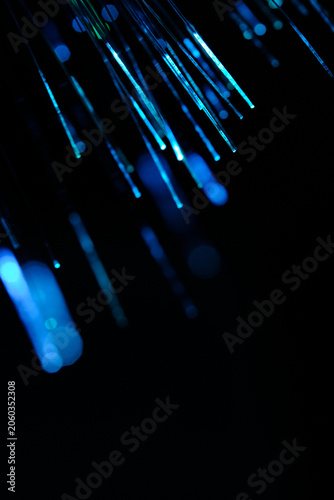 Vertical presentation glowing light blue fiber optic threads radiating against dark background.