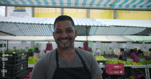 Εκτύπωση καμβά Hispanic street vendor smiling in close portrait at outdoor produce market evoki