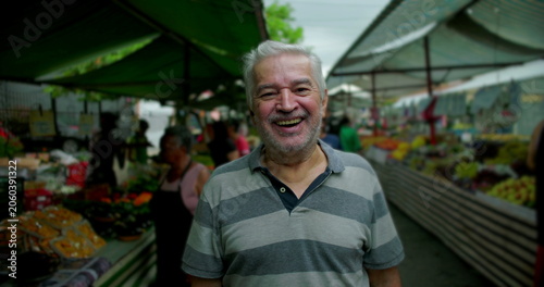 Foto Elderly man standing at outdoor street market looking at camera with gentle smil