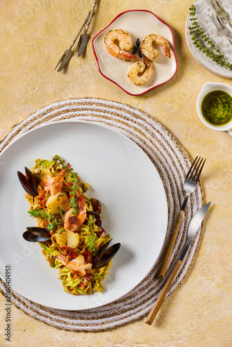 A top-down, flat lay shot of a gourmet seafood pasta dish served on a white ceramic plate