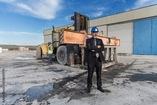  Construction senior boss in outdoors image near to bulldozer and work woman, Cordoba, Spain.