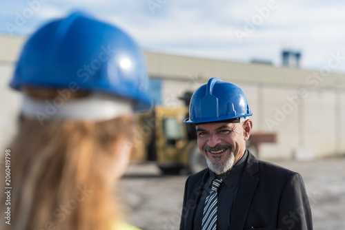 Senior boss talking to young female worker at concrete factory outdoors. Cordoba, Spain.
