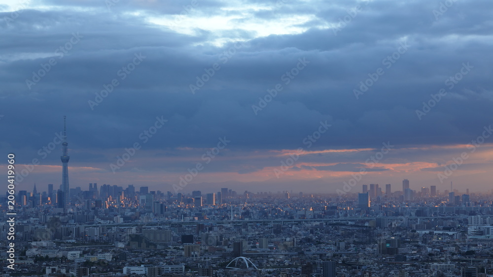 Fototapeta premium 夕陽に照らされた都市の風景 雨雲が残る空に広がる幻想的な光景 / Cityscape Illuminated by Sunset Beneath Rain Clouds in a Dramatic Evening Sky