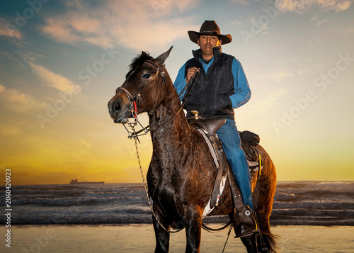 A cowboy sitting on a a brown horse at sunset