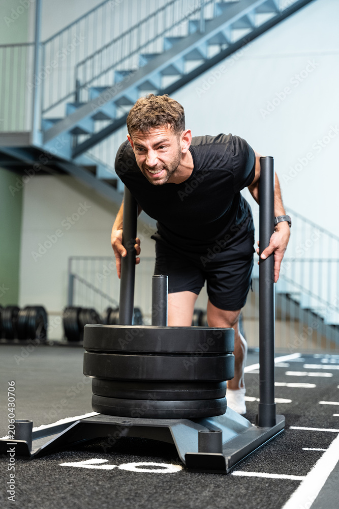 Obraz premium Determined man pushing heavy sled during intense gym workout