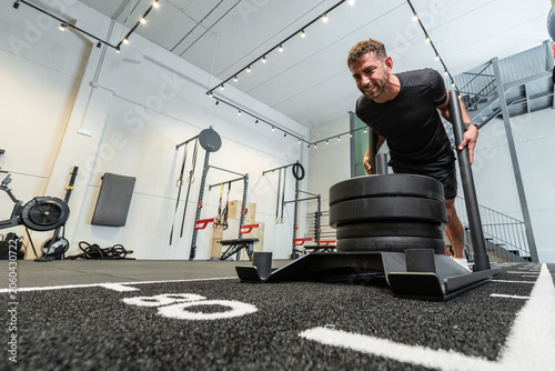 Strong man pushing weighted sled in modern gym