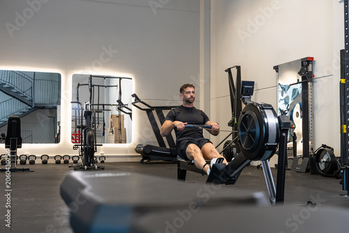 Determined man training on rowing machine in modern gym