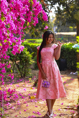 Indian young cute woman style pink dressed standing posing for a photoshoot. pink flowering garden in the park background at springtime.