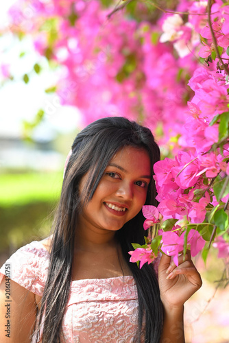 Portrait of a Indian young woman in a pink dressed, standing in a spring blooming rented park. hands holding on a pink cherry flowers.