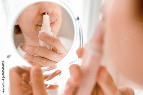Fotografie A man uses an electric trimmer for nose hair removal while looking in a mirror