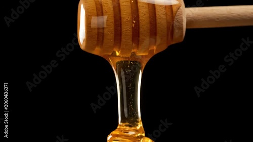 Golden Honey Dripping from Wooden Dipper on Black Background.