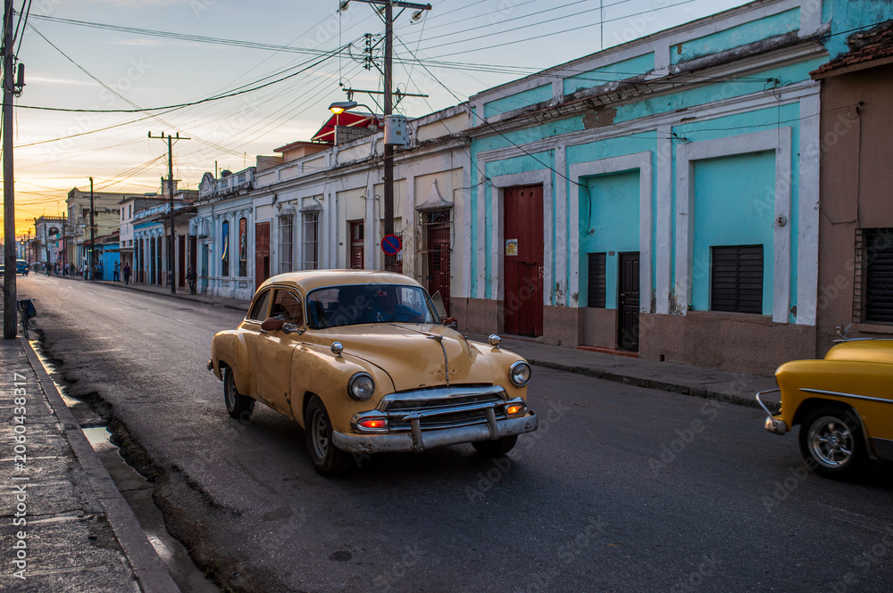 Fototapeta premium Yellow vintage car driving through a street in Cienfuegos