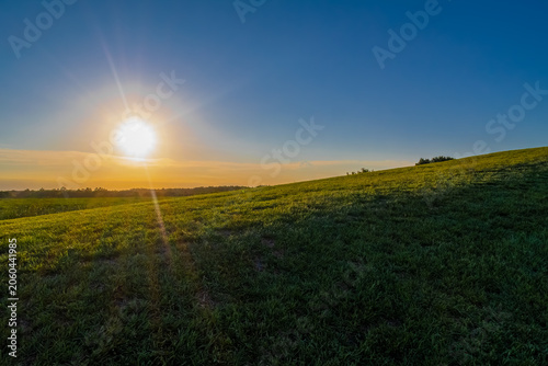 Fotografie Sunset over a green hilltop