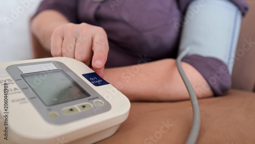 Senior woman checking blood pressure at home with a digital tonometer on her arm, emphasizing self care, prevention, daily monitoring and independent health management