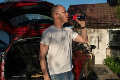 Spragniona osoba pije napój w przerwie w pracy przy samochodzie