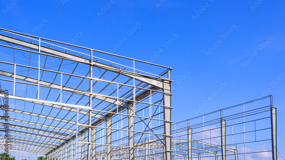 Naklejka premium Metal framework of industrial warehouse buildings structure in construction site against blue sky background, low angle view