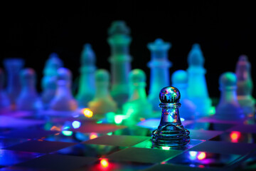 Clear glass pawn piece on a chessboard illuminated by colourful fairy lights with a blurred background of frosted glass pieces