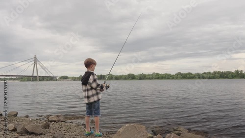 A little boy is fishing on a big river using a spinning rod