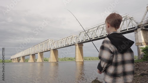 A little boy is fishing on a big river using a spinning rod