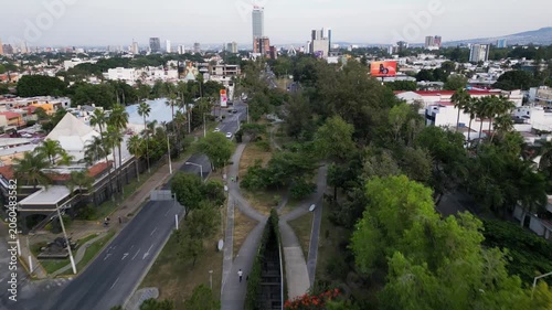 Guadalajara, Mexico - November 16 2025: Backward drone footage captures Lazaro Cardenas Linear Park, an urban street, gas station, Sanborns, and Guadalajara city