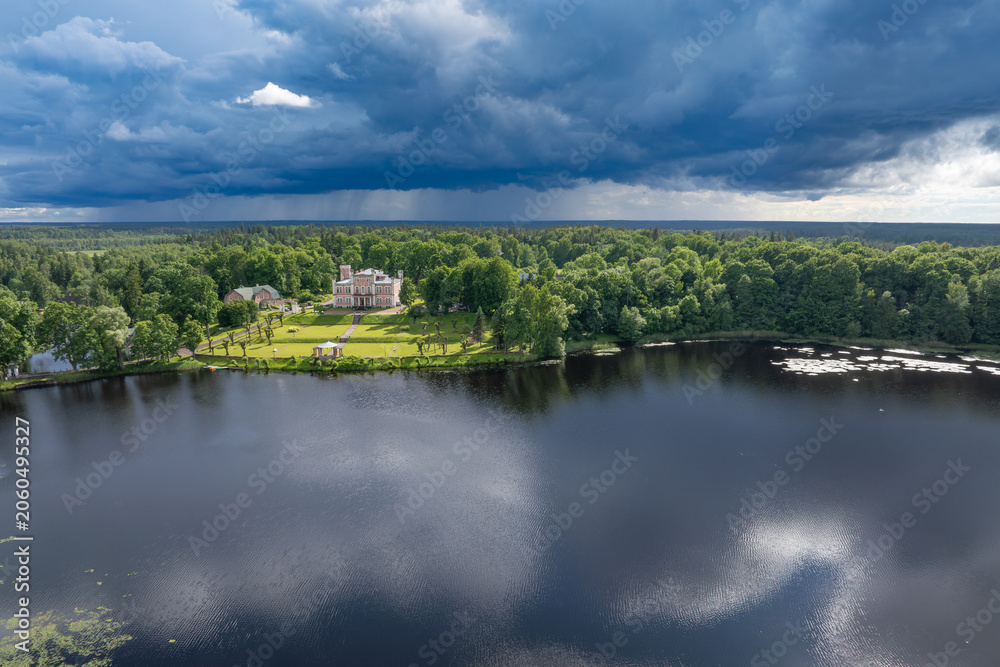Fototapeta premium Birini Castle and Lake Birini beneath an approaching summer thunderstorm, aerial view of Latvia