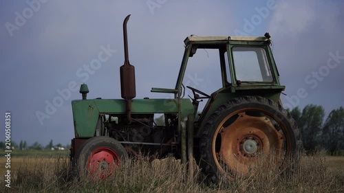 An old tractor standing in a field in swaying grass while the sunlight breaks through the clouds.