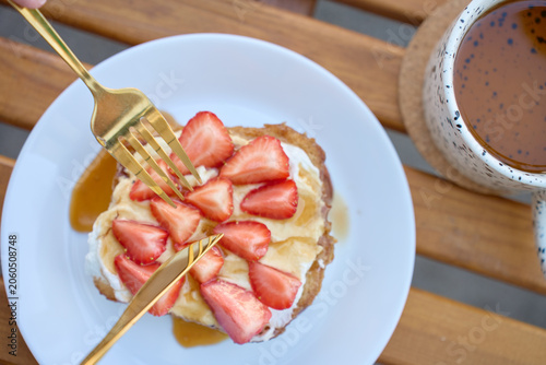 French toast with strawberries, yogurt and honey is served with tea on wooden table