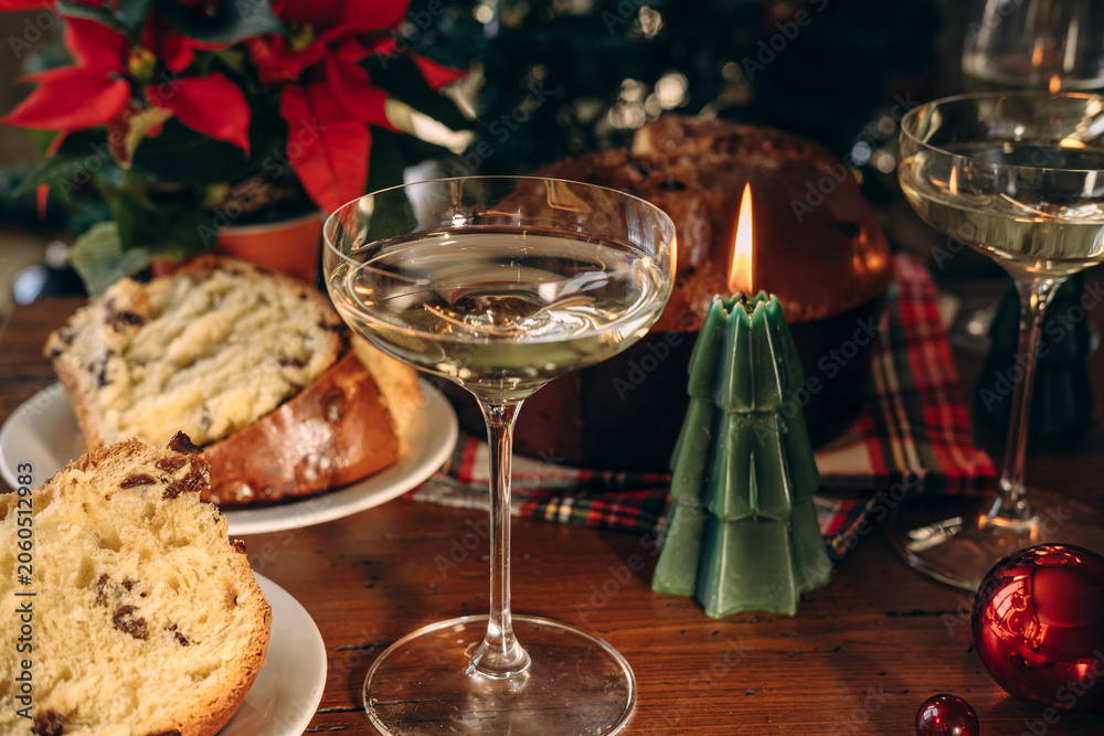 Fototapeta premium Christmas Table With Panettone, Champagne Glasses and Green Tree Candle Beside Poinsettia