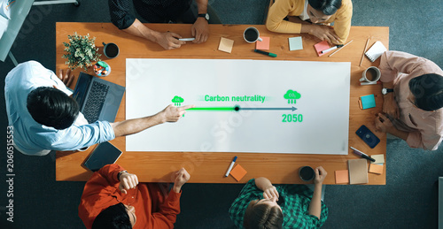 Valokuva A diverse group of professionals engages in a focused discussion about strategies and goals for achieving carbon neutrality by 2050 in a modern office setting