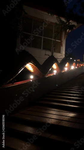 Panning up an ornate Naga banister over a staircase leading up to a golden Buddha. Taken at night with dramatic lighting under the serpent giving Buddha a dramatic entry.
