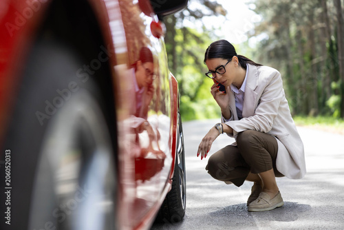 Foto Woman crouching by her red car on a roadside calling for assistance, dealing wit