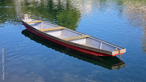 Foto Traditional wooden riverboat with red hull moored on calm blue water surface