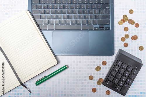 Top view of a laptop keyboard, coins, a pen, and a notebook with blank pages.