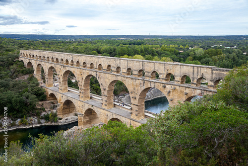 Aerial view of the complete Pont du Gard Roman aqueduct spanning the Gardon River amid lush green woodland in southern France