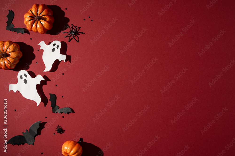 Fototapeta premium Happy Halloween scene with paper ghost cutouts, mini pumpkins and black bat decorations on red background