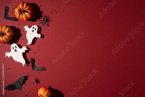 Happy Halloween scene with paper ghost cutouts, mini pumpkins and black bat decorations on red background