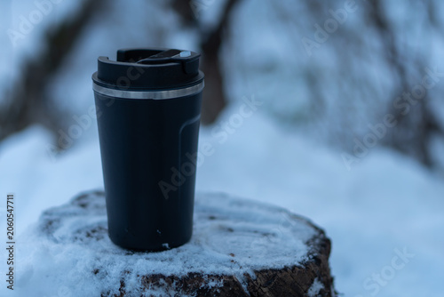 A hot drink in a thermal mug amidst a snowy forest setting.