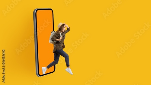 Fotografie Joyful Young Asian Woman Stepping Out Of Smartphone With Bright Yellow Background, Embarking On A New Adventure Full Of Possibilities