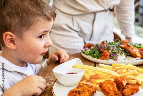 Little boy eating chicken nuggets and french fries at a restaurant table