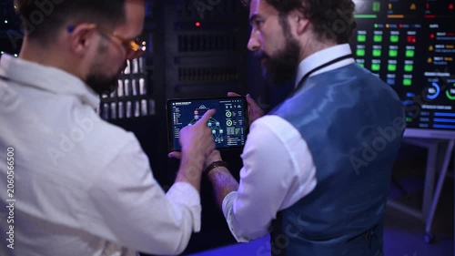 Two male it engineers analyzing network infrastructure on a tablet in a modern data center server room