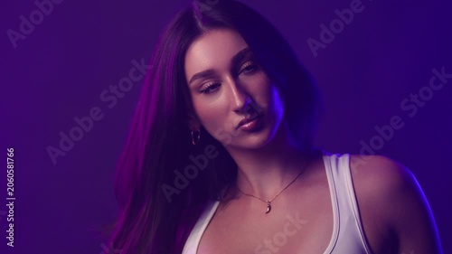 Confident young woman with dark hair and bold makeup in studio lighting, fashion and beauty portrait. The woman looks directly at the viewer with a serious expression. Her long dark hair frames her fa