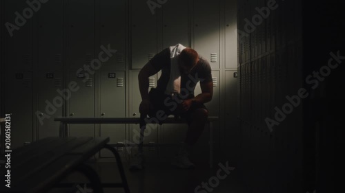 Following Intense Session, Athlete With Limb Loss Retreats to Dressing Room to Restore Energy. Man Sits Down Wearily, Leaning Against Lockers as Beam of Natural Light Fills Space. Inclusive Wellness.