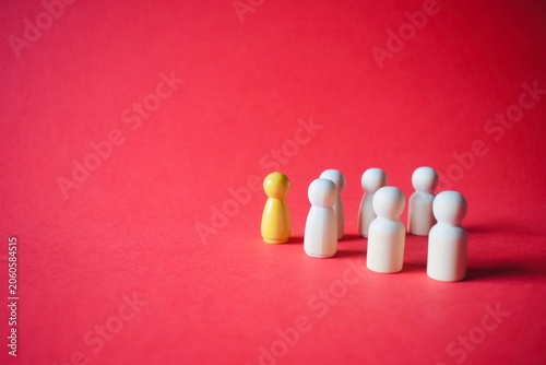 Cuadro en lienzo A single yellow wooden peg doll leading a group of white peg dolls on a vibrant red background, conceptualizing leadership, individuality, and team management