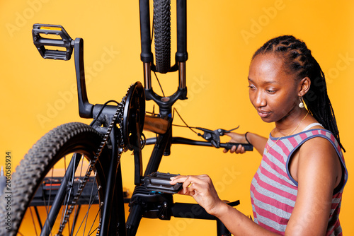 Tableau sur toile Determined African American lady seen checking bike for damages with keen eye for detail, young Black woman inspects bike pedals and brakes ensuring smooth and efficient outdoor cycling