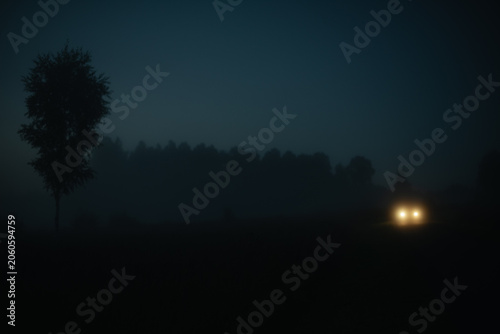 Car headlights glowing through dense fog at night